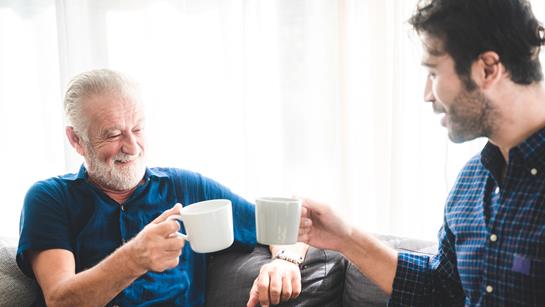 Older Man Happy At Home With A Younger Man Holding A Cup Of Tea